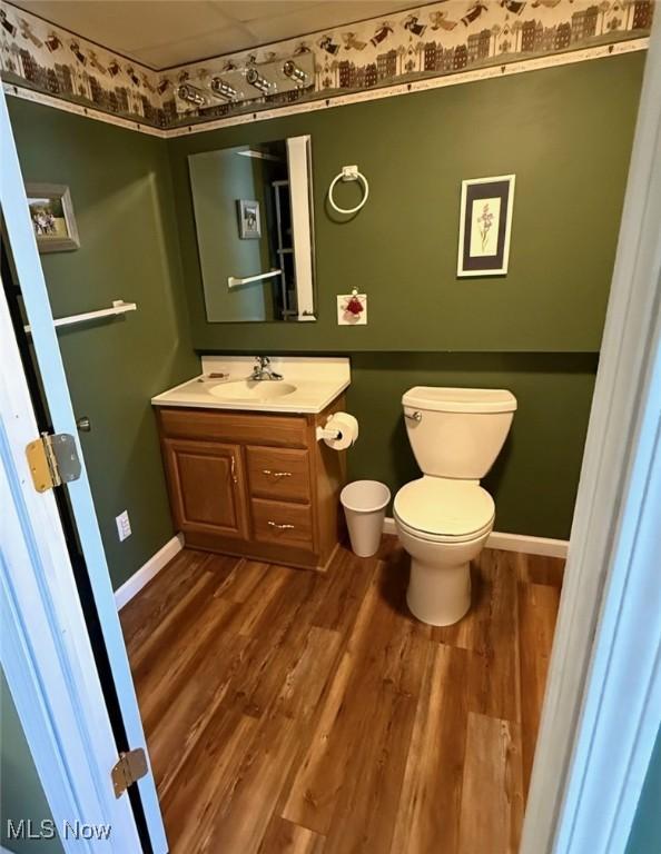 half bath with toilet, baseboards, wood finished floors, and vanity