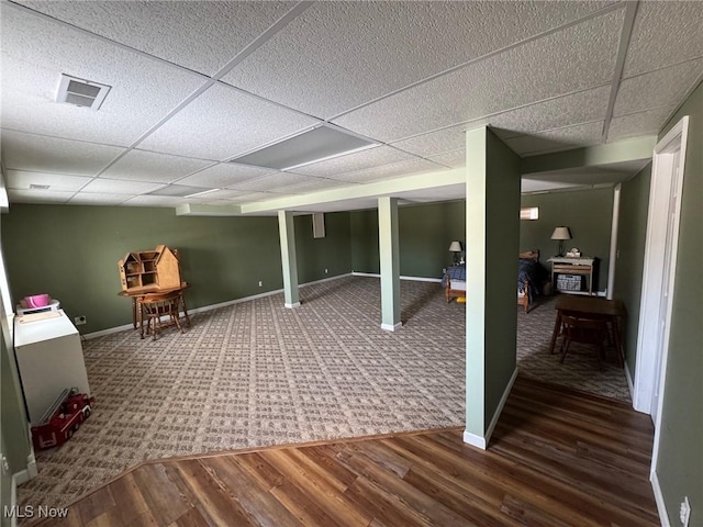 finished basement with a paneled ceiling, dark wood finished floors, visible vents, and baseboards