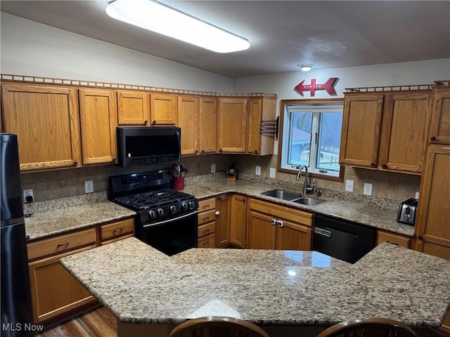 kitchen featuring light stone countertops, black appliances, brown cabinets, and a sink