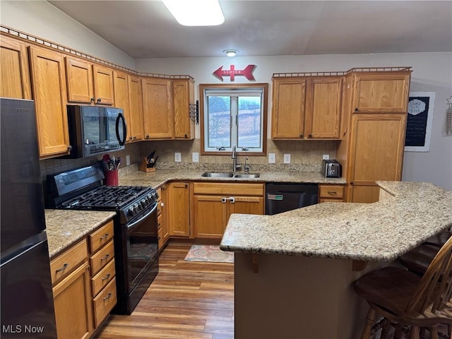 kitchen with light stone counters, a kitchen breakfast bar, light wood-type flooring, black appliances, and a sink