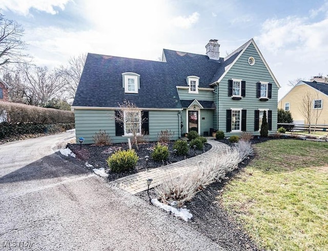 view of front of house with roof with shingles, a chimney, and a front lawn