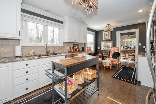 kitchen with dark stone countertops, white cabinets, a notable chandelier, and a sink