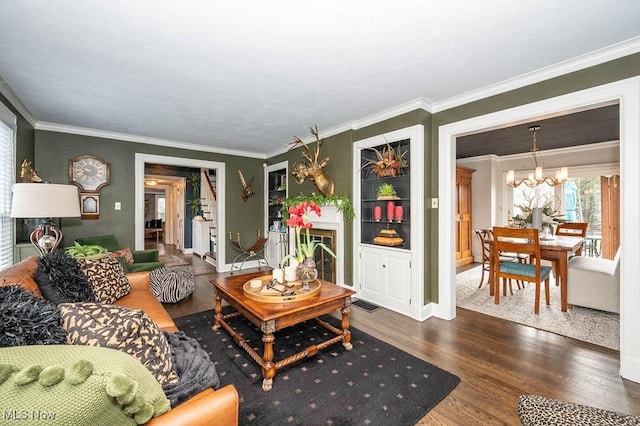 living room with a chandelier, wood finished floors, visible vents, baseboards, and ornamental molding