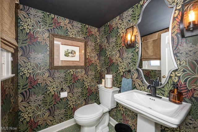 half bathroom with baseboards, toilet, and wallpapered walls