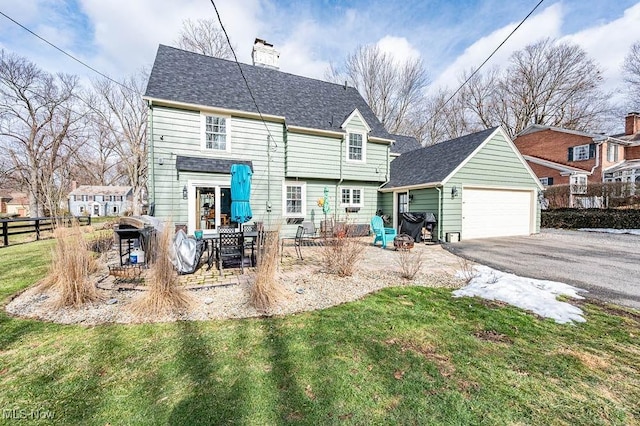 back of house featuring a garage, an outdoor structure, fence, a lawn, and a chimney