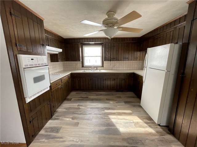 kitchen featuring under cabinet range hood, white appliances, a sink, light countertops, and light wood finished floors