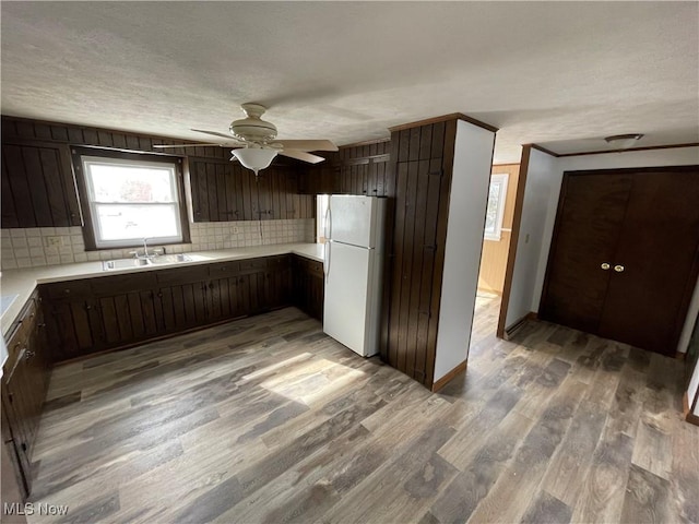 kitchen with light countertops, decorative backsplash, freestanding refrigerator, a sink, and wood finished floors