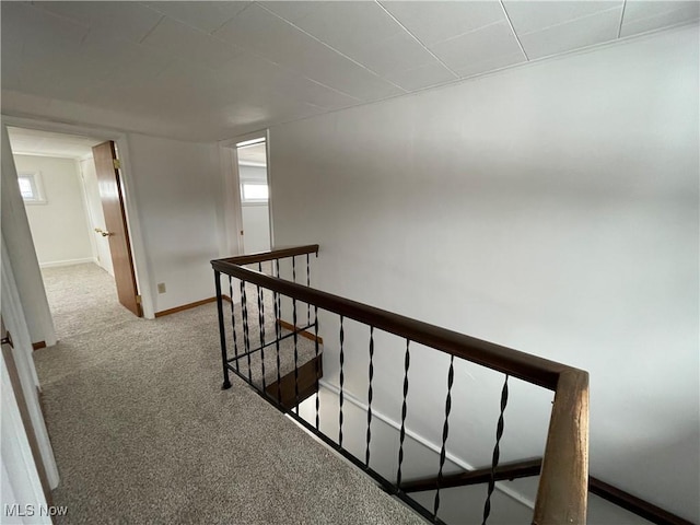 corridor featuring carpet, a healthy amount of sunlight, baseboards, and an upstairs landing