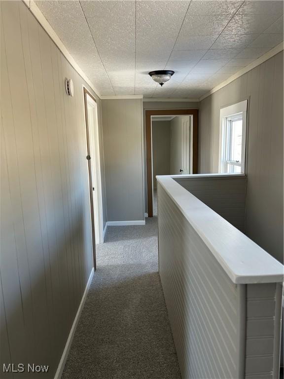 corridor featuring wooden walls, baseboards, an upstairs landing, a textured ceiling, and carpet flooring