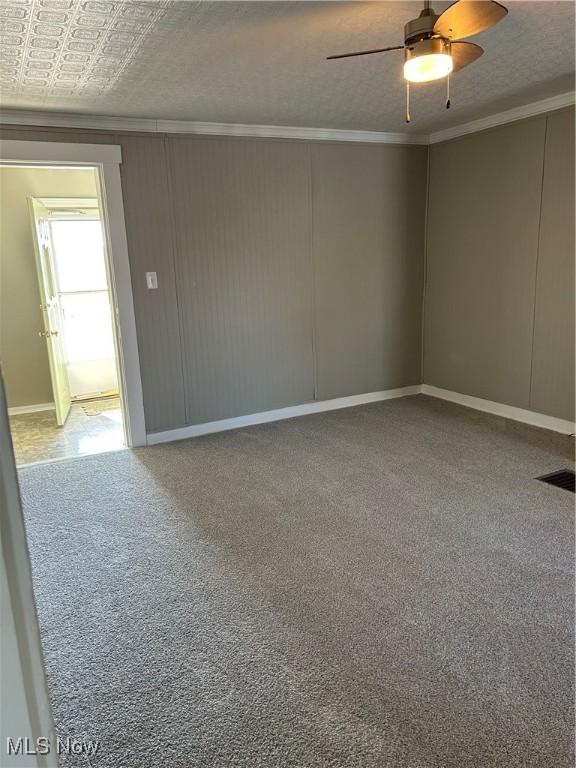 carpeted spare room featuring ornamental molding, visible vents, a textured ceiling, and a ceiling fan