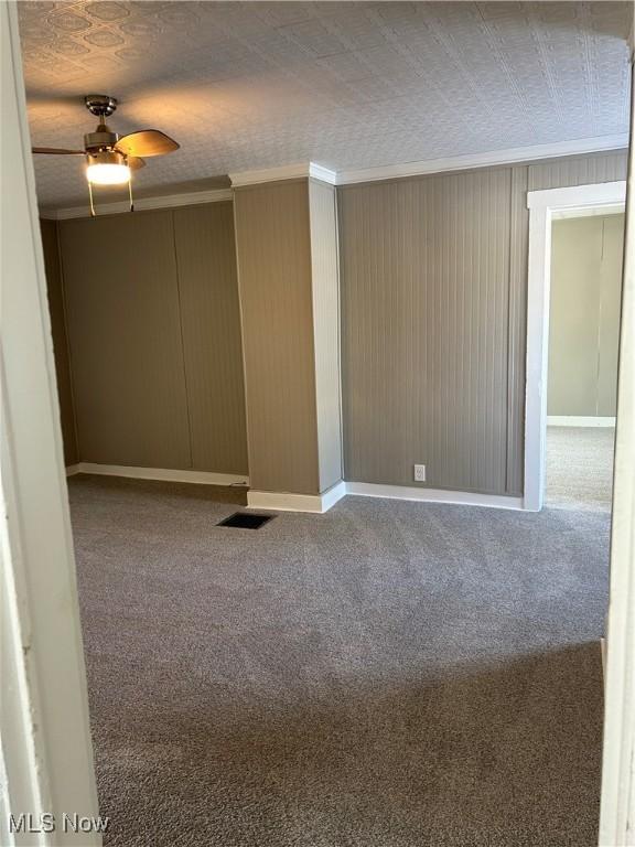 carpeted empty room with ceiling fan, a textured ceiling, visible vents, and crown molding