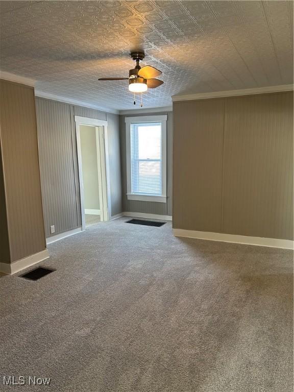 spare room featuring baseboards, carpet flooring, visible vents, and crown molding