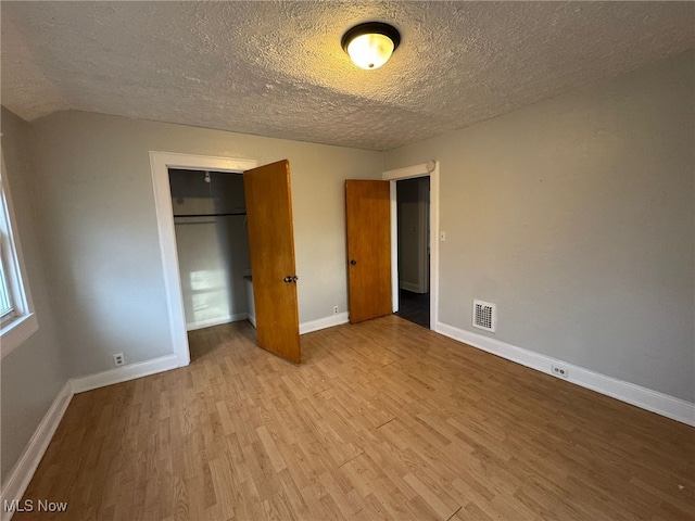 unfurnished bedroom with a textured ceiling, visible vents, baseboards, a closet, and light wood finished floors