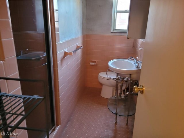 full bath featuring toilet, a sink, tile walls, tile patterned floors, and a stall shower