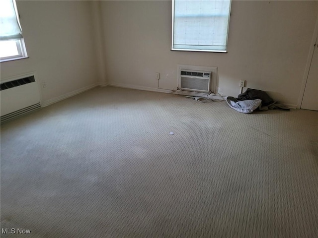 carpeted spare room featuring a wall unit AC and radiator heating unit