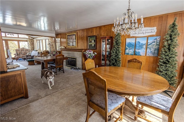 carpeted dining area featuring a fireplace, an inviting chandelier, and wooden walls