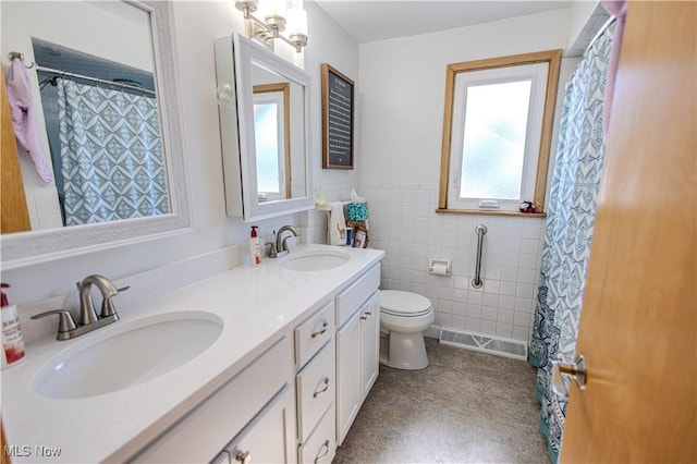 bathroom featuring a wainscoted wall, double vanity, a sink, and tile walls