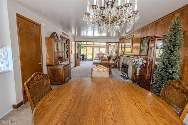 dining space with baseboards, light colored carpet, a fireplace with flush hearth, an inviting chandelier, and wood walls