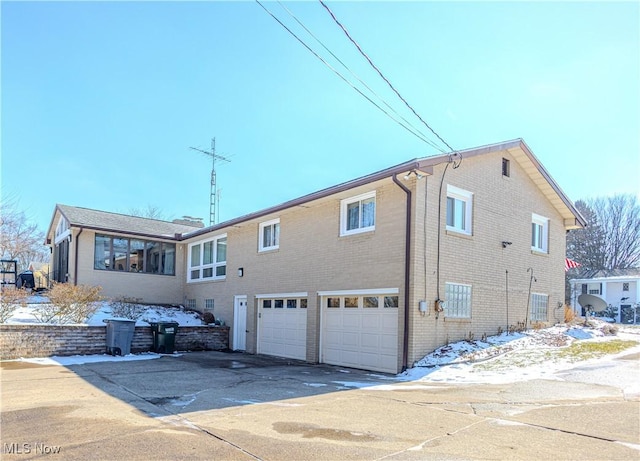 snow covered rear of property with driveway, brick siding, and an attached garage