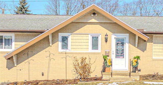 view of front of home with entry steps, brick siding, and roof with shingles