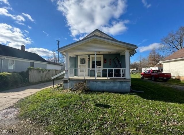 view of front of property featuring covered porch, fence, and a front lawn