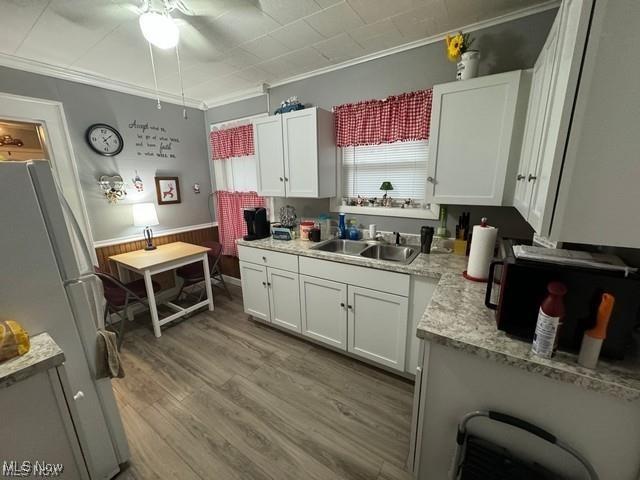 kitchen with crown molding, freestanding refrigerator, white cabinetry, and a sink