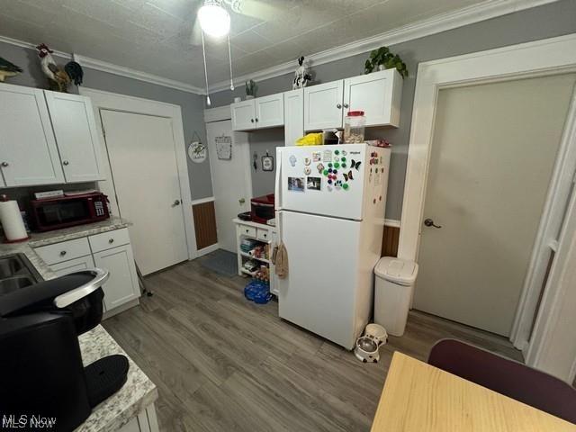 kitchen with freestanding refrigerator, white cabinetry, crown molding, and wood finished floors