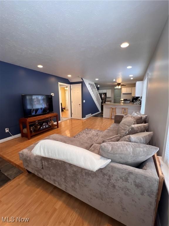 living area with light wood finished floors, baseboards, stairs, a textured ceiling, and recessed lighting