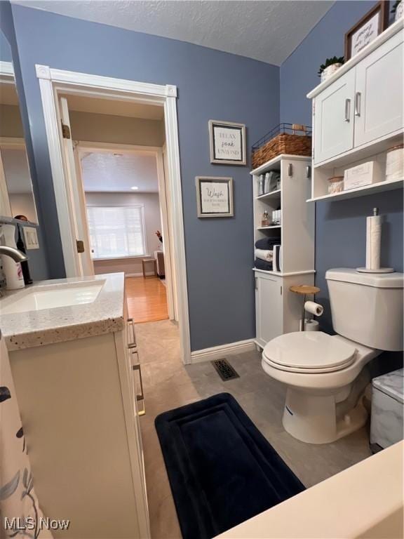 bathroom with baseboards, a textured ceiling, toilet, and vanity