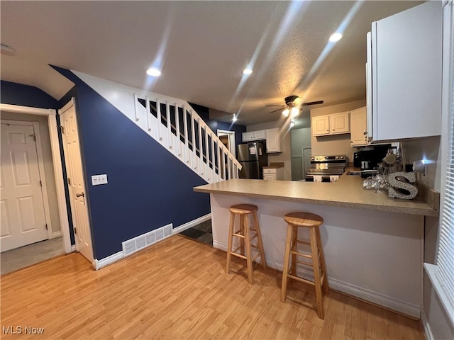 kitchen featuring visible vents, light wood-style flooring, freestanding refrigerator, stainless steel range with electric cooktop, and a peninsula