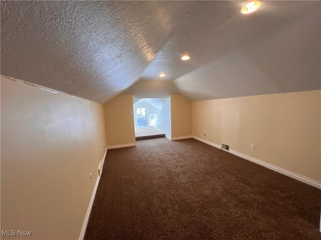 additional living space featuring lofted ceiling, baseboards, visible vents, and dark carpet