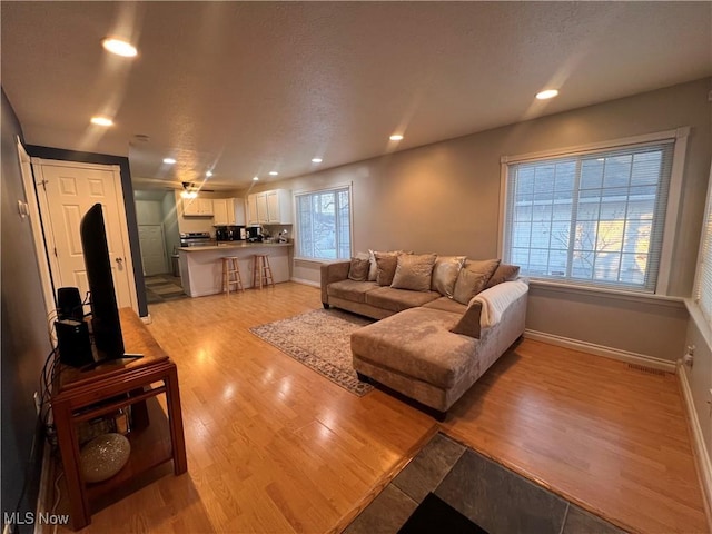 living area featuring light wood finished floors, baseboards, visible vents, a textured ceiling, and recessed lighting