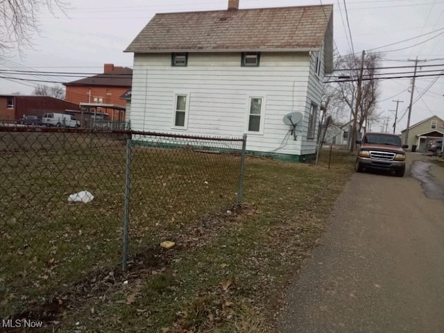 view of side of property featuring roof with shingles, a yard, a chimney, and fence