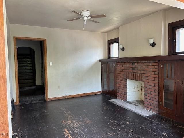 unfurnished living room with a fireplace, a ceiling fan, and baseboards