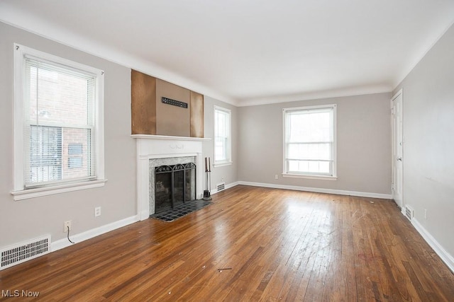 unfurnished living room featuring dark wood-type flooring, a premium fireplace, visible vents, and baseboards