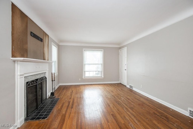 unfurnished living room with a tiled fireplace, dark wood finished floors, visible vents, and baseboards