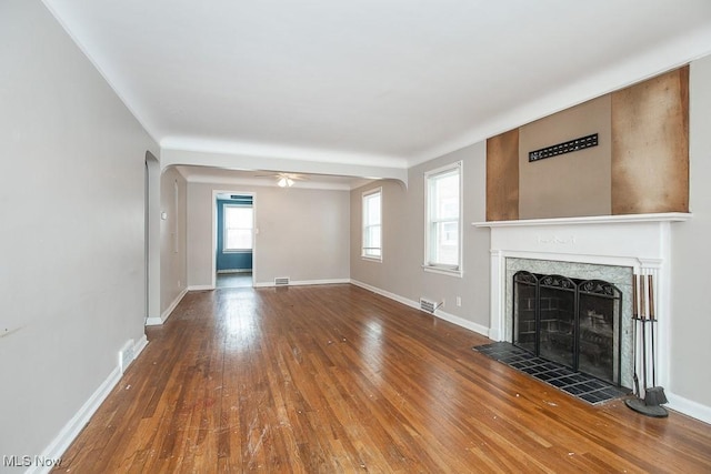 unfurnished living room with a fireplace, baseboards, arched walkways, and wood finished floors