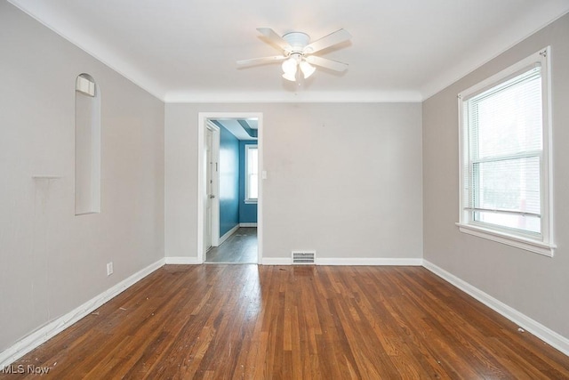 empty room featuring dark wood-type flooring, visible vents, baseboards, and a ceiling fan