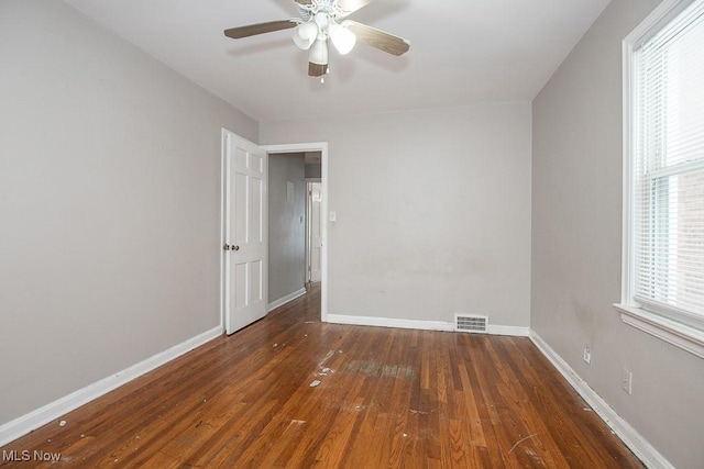 empty room with baseboards, visible vents, dark wood finished floors, and a wealth of natural light