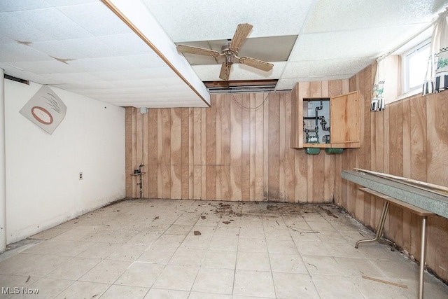 basement with ceiling fan and wooden walls