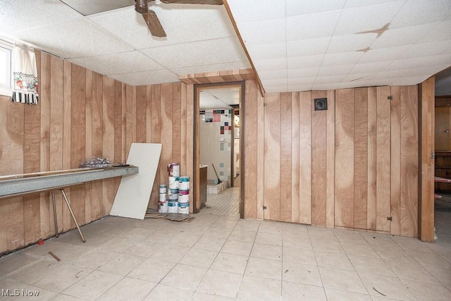 finished below grade area with ceiling fan, wooden walls, and a drop ceiling