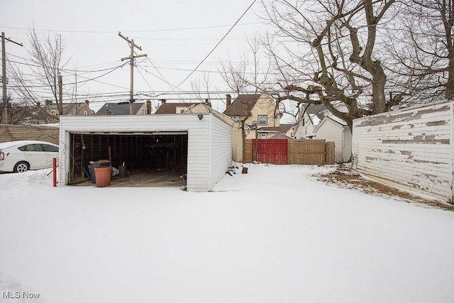 snow covered garage featuring a detached garage and fence