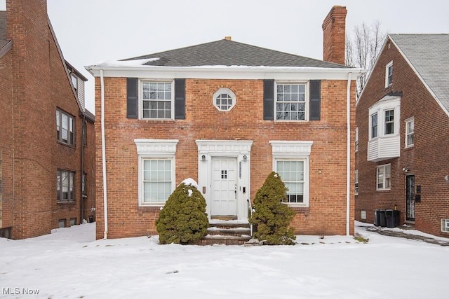 colonial inspired home featuring brick siding, a chimney, and central AC unit