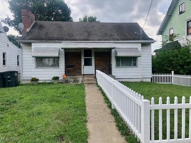 bungalow-style home featuring a chimney, roof with shingles, a fenced front yard, and a front yard