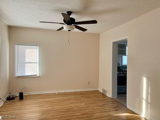 empty room featuring baseboards, visible vents, a textured ceiling, and light wood finished floors