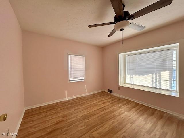 empty room with light wood-style floors, ceiling fan, visible vents, and baseboards