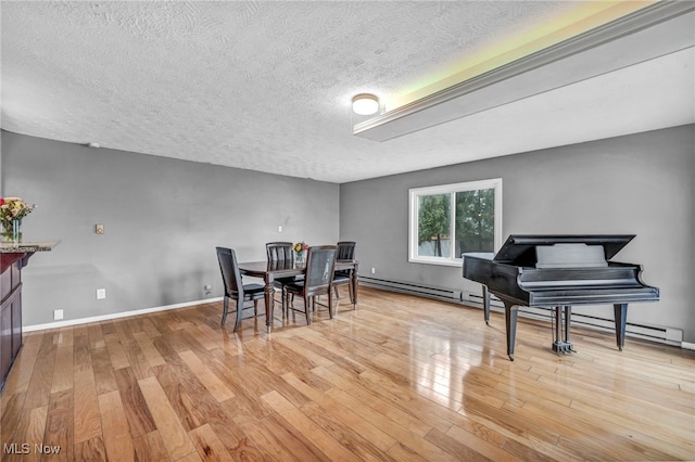 dining room with a baseboard heating unit, light wood-style flooring, baseboards, and a textured ceiling