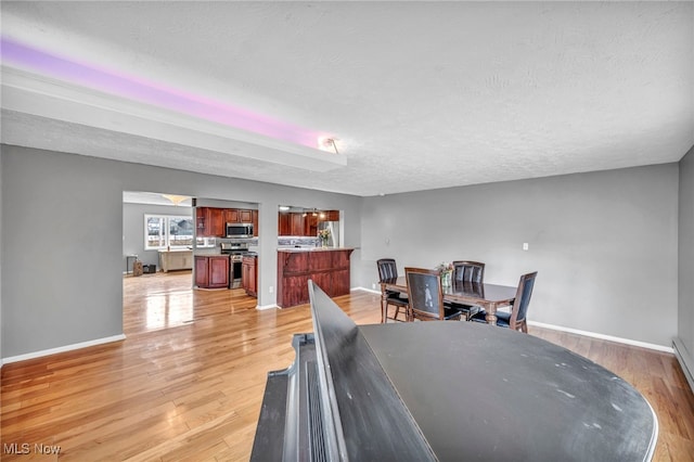 dining room with light wood-style floors, a textured ceiling, and baseboards