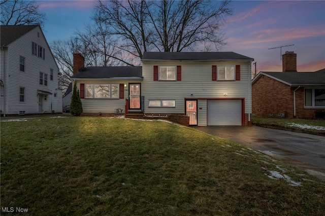 split level home with a garage, a chimney, concrete driveway, and a front yard