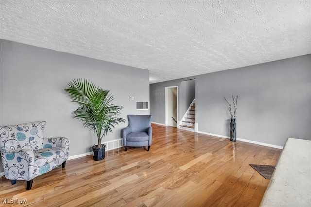 living area featuring a textured ceiling, wood finished floors, visible vents, baseboards, and stairway